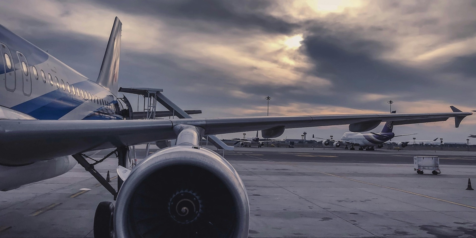 Flugzeuge am Flughafen im Abendlicht, Wolken und ein Triebwerk im Vordergrund